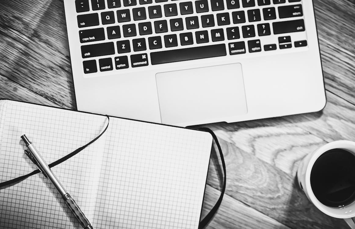 A black-and-white photo of a laptop and a notebook.