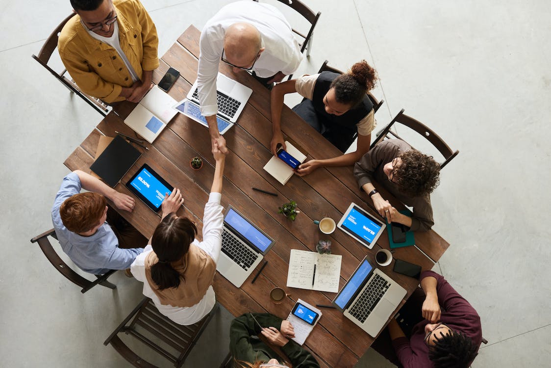 People working on computers around a table as two shake hands.